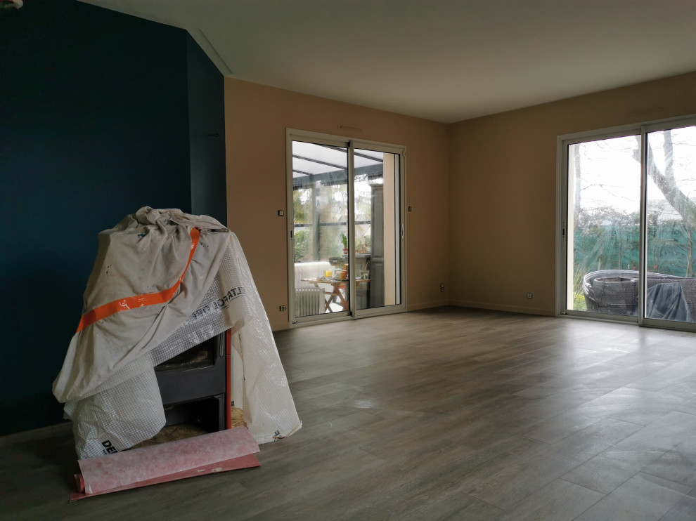 Immagine di un soggiorno minimalista di medie dimensioni e aperto con sala formale, pareti beige, pavimento in laminato, stufa a legna, cornice del camino in metallo, TV a parete e pavimento grigio