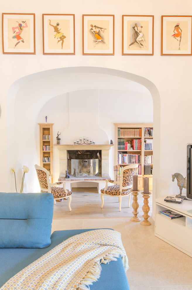 Cette photo montre un salon méditerranéen avec un mur blanc, un sol en carrelage de céramique, un sol beige, une bibliothèque ou un coin lecture, une cheminée standard, un manteau de cheminée en pierre et un téléviseur indépendant.