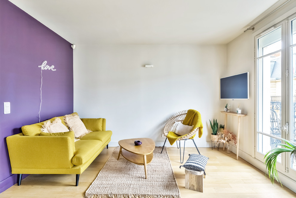 Modelo de salón abierto actual de tamaño medio sin chimenea con paredes blancas, suelo de madera clara, televisor colgado en la pared y suelo marrón