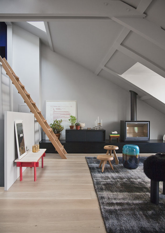 Modelo de salón tipo loft actual de tamaño medio sin televisor con paredes grises, suelo de madera clara y estufa de leña
