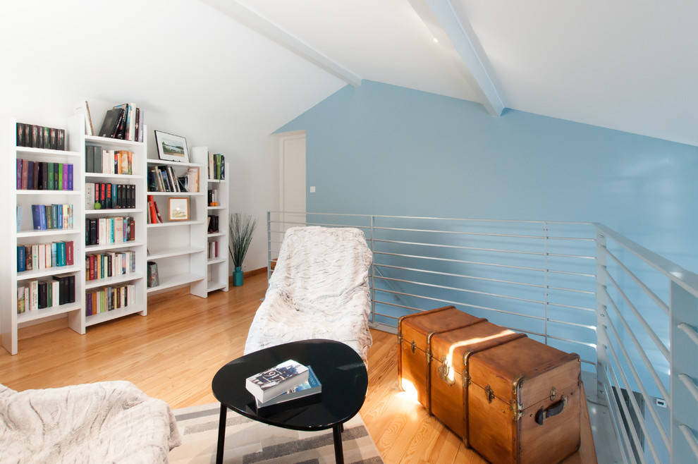 Cette image montre un grand salon design ouvert avec une bibliothèque ou un coin lecture, un mur bleu, parquet clair et un poêle à bois.