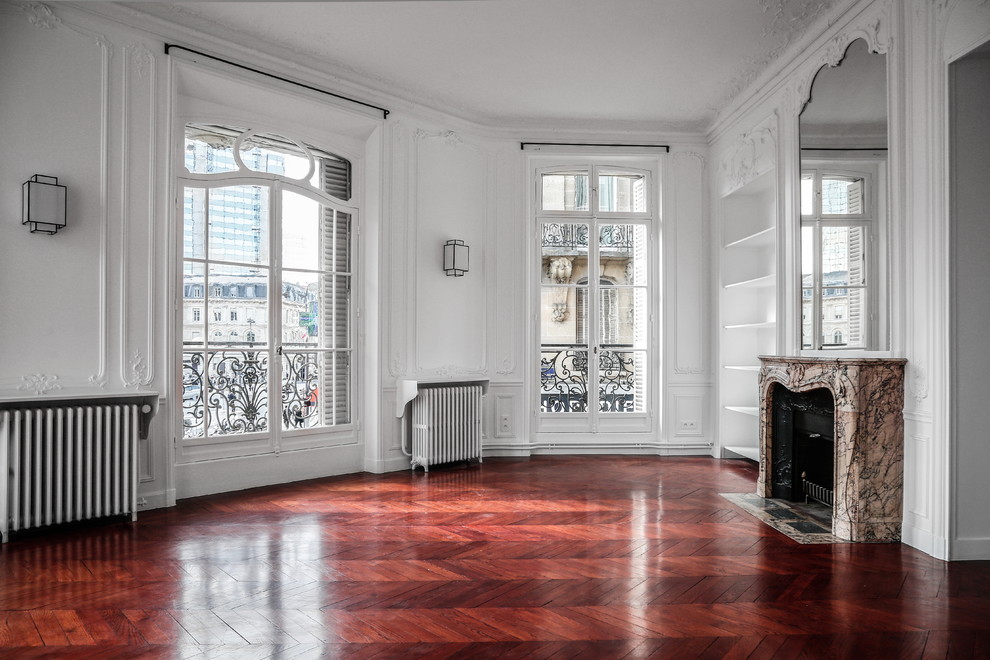 Großes, Repräsentatives Klassisches Wohnzimmer mit weißer Wandfarbe, dunklem Holzboden, Kaminumrandung aus Stein und rotem Boden in Paris