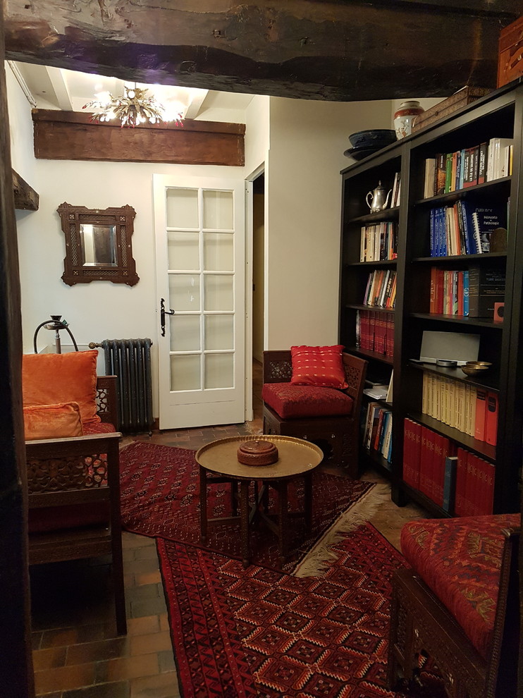 Esempio di un piccolo soggiorno bohémian aperto con libreria, pareti bianche, pavimento in terracotta, nessun camino, nessuna TV e pavimento marrone