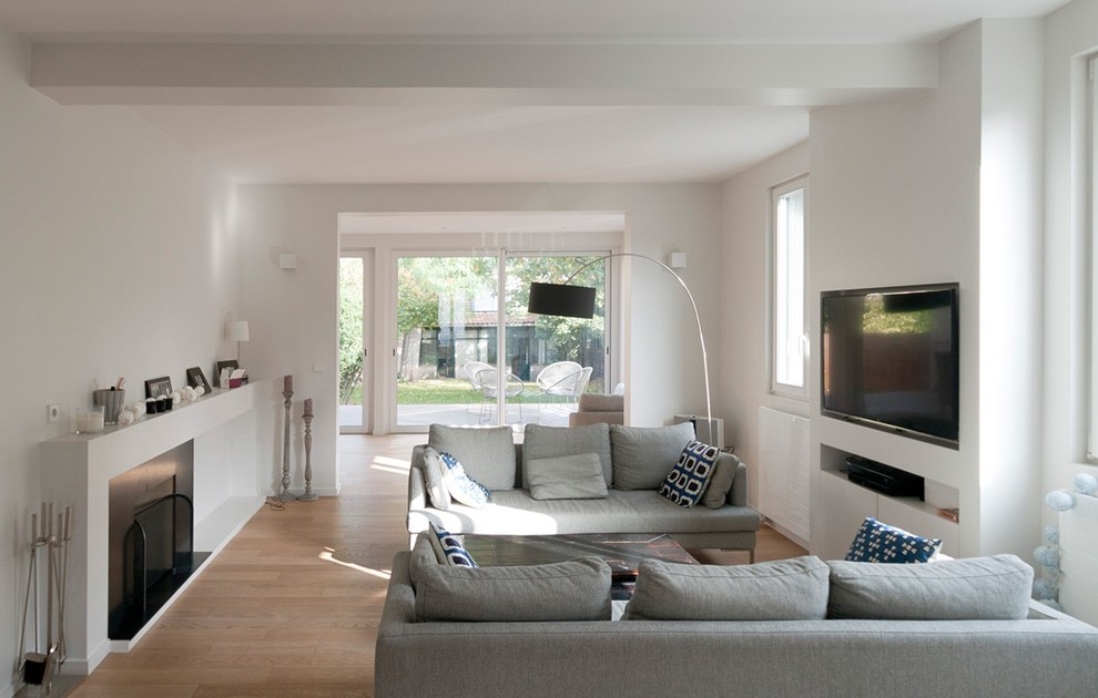 Cette image montre un salon design de taille moyenne et fermé avec un mur blanc, parquet clair, une cheminée standard, un téléviseur fixé au mur et éclairage.