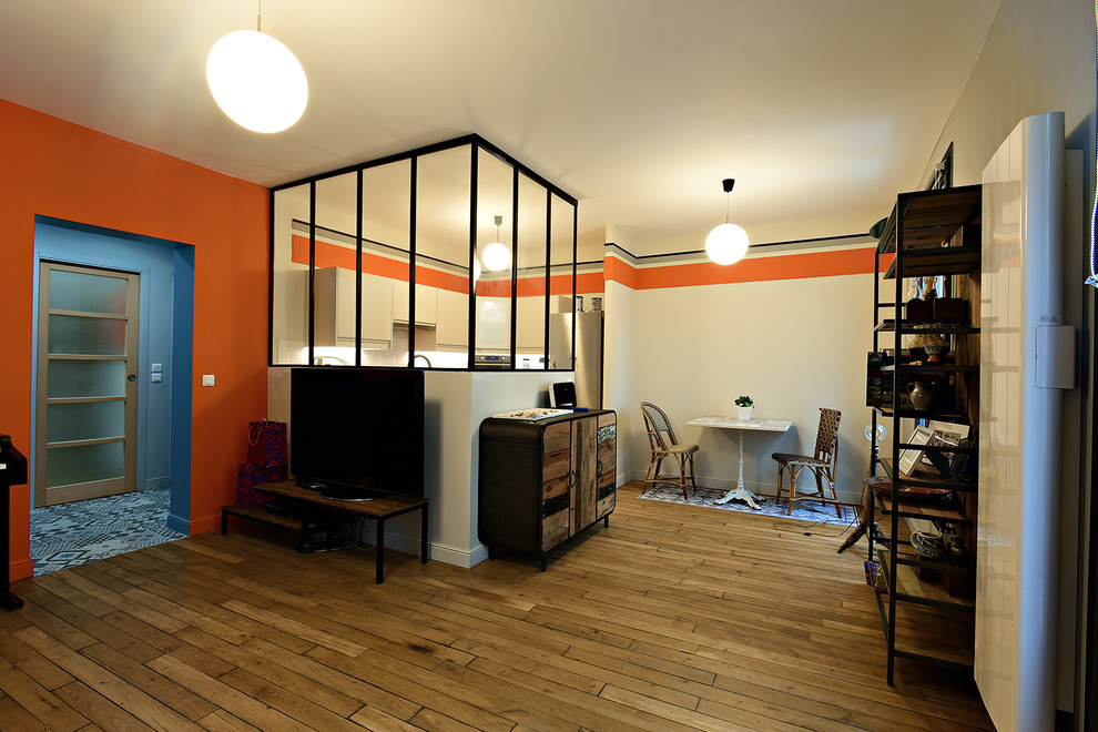Modern inredning av ett stort allrum med öppen planlösning, med ett bibliotek, orange väggar, ljust trägolv, en fristående TV och beiget golv