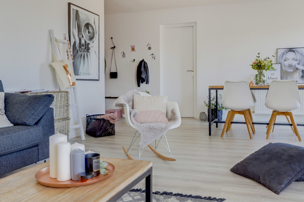 Mittelgroßes, Offenes Nordisches Wohnzimmer mit weißer Wandfarbe, Laminat, Kaminumrandung aus Holz, freistehendem TV und grauem Boden in Lyon