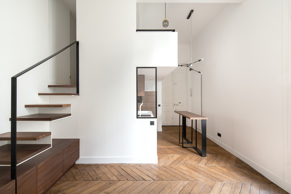 Kleines, Offenes Modernes Wohnzimmer ohne Kamin mit weißer Wandfarbe, braunem Holzboden, verputzter Kaminumrandung, verstecktem TV und braunem Boden in Paris