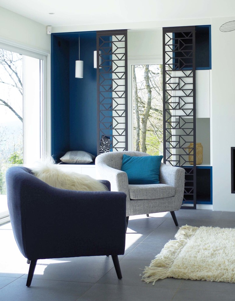 Идея дизайна: гостиная комната среднего размера в современном стиле с с книжными шкафами и полками, синими стенами, стандартным камином, фасадом камина из штукатурки, телевизором на стене и серым полом