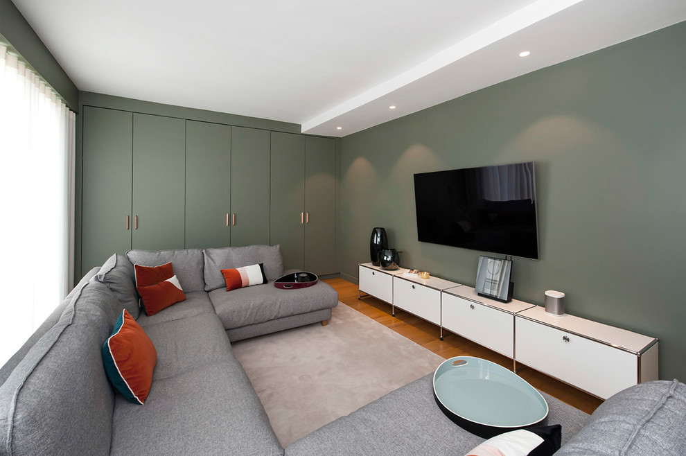 Immagine di un grande soggiorno minimal aperto con pareti verdi, TV a parete, nessun camino, libreria, parquet chiaro e pavimento marrone