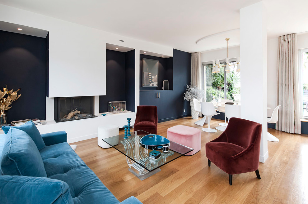 Стильный дизайн: большая открытая гостиная комната в современном стиле с синими стенами, светлым паркетным полом, подвесным камином, фасадом камина из штукатурки и белым полом без телевизора - последний тренд