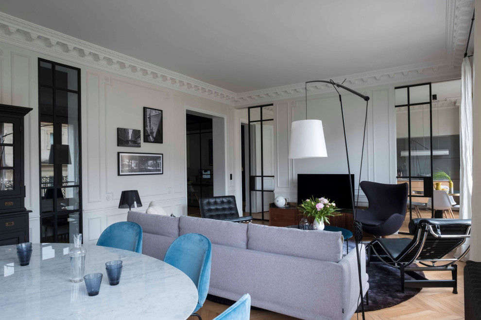 Modelo de salón abierto actual grande con paredes blancas, suelo de madera clara, televisor independiente y suelo beige
