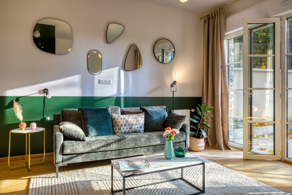 На фото: открытая гостиная комната среднего размера в стиле неоклассика (современная классика) с зелеными стенами, светлым паркетным полом, отдельно стоящим телевизором и коричневым полом