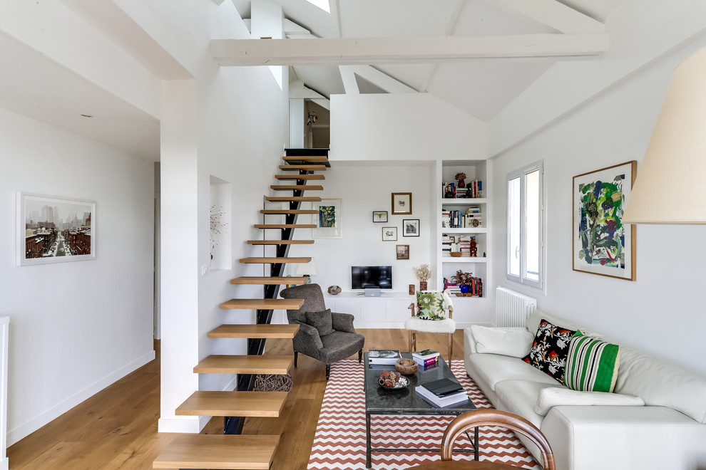 Diseño de biblioteca en casa abierta contemporánea de tamaño medio sin chimenea con paredes blancas, suelo de madera en tonos medios y televisor independiente