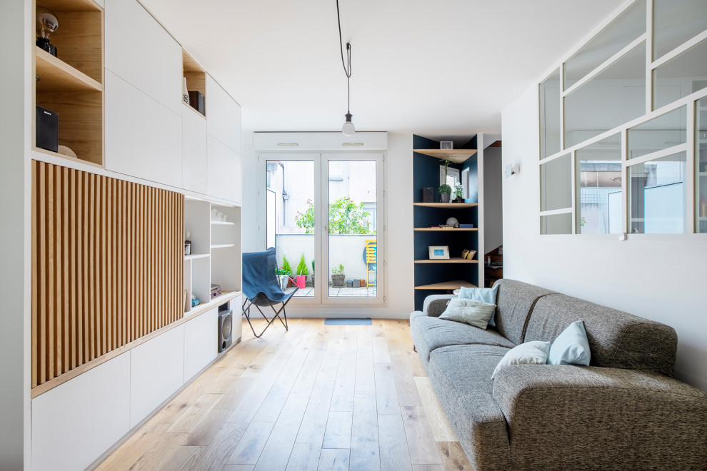 Exempel på ett mellanstort minimalistiskt allrum med öppen planlösning, med ett bibliotek, vita väggar, ljust trägolv, en väggmonterad TV och beiget golv