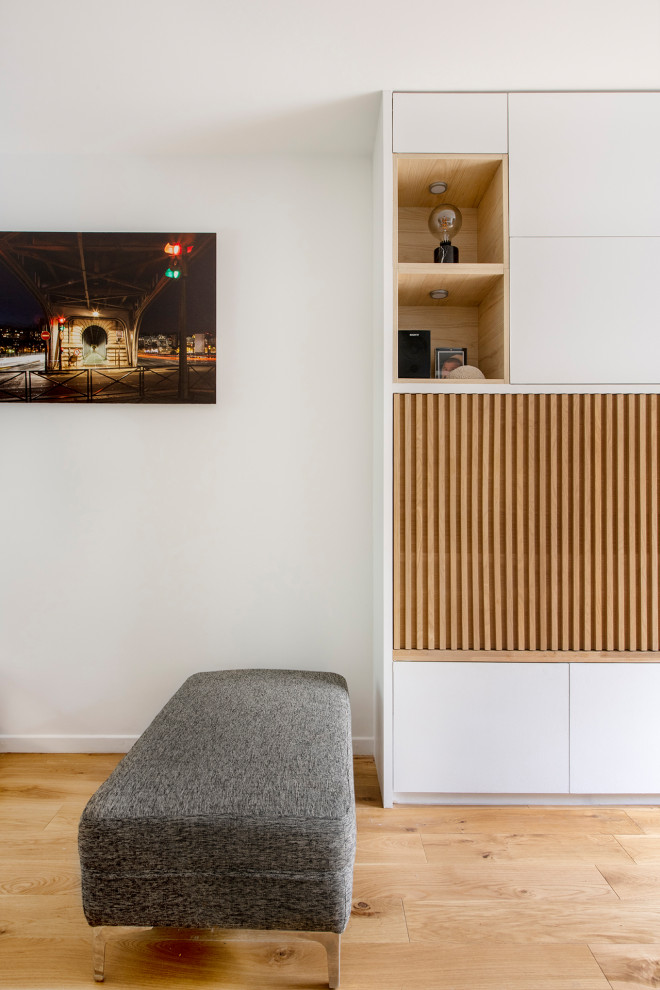 Стильный дизайн: открытая гостиная комната среднего размера в скандинавском стиле с с книжными шкафами и полками, белыми стенами, светлым паркетным полом, телевизором на стене и бежевым полом без камина - последний тренд