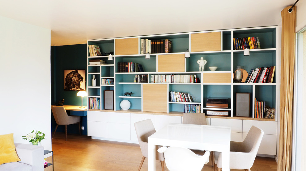 Inredning av ett modernt mellanstort allrum med öppen planlösning, med ett bibliotek, blå väggar, ljust trägolv, brunt golv och en dold TV