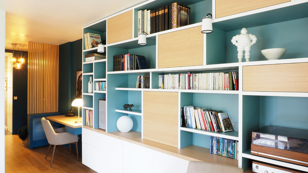Mittelgroße, Offene Moderne Bibliothek mit blauer Wandfarbe, hellem Holzboden, braunem Boden und verstecktem TV in Paris