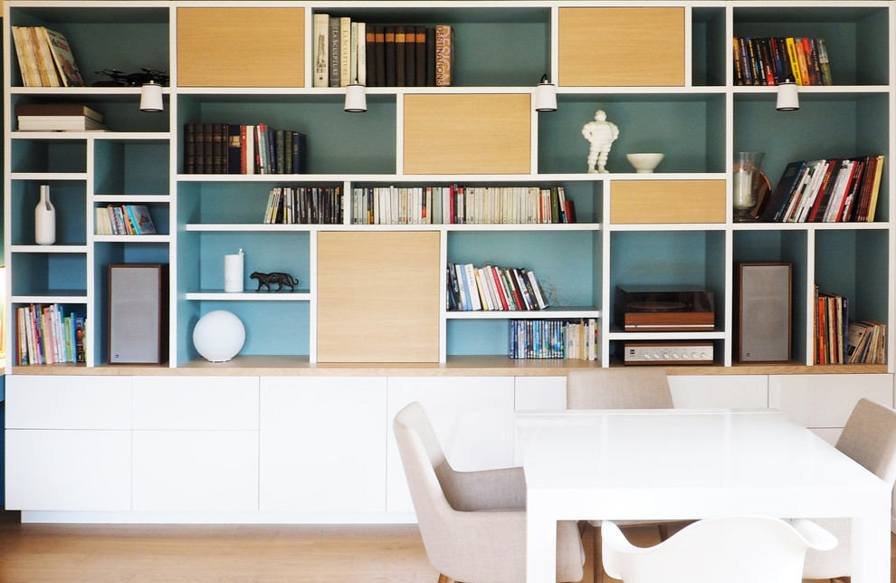 Diseño de biblioteca en casa abierta contemporánea de tamaño medio con paredes azules, suelo de madera clara, televisor retractable y suelo marrón
