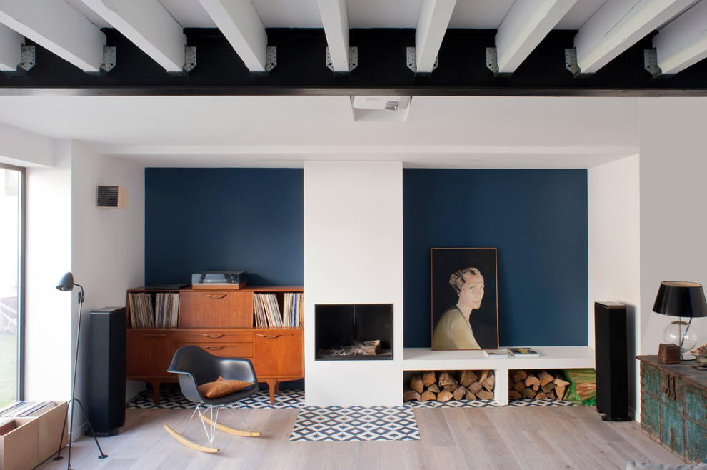 Große, Abgetrennte Moderne Bibliothek mit blauer Wandfarbe, hellem Holzboden, Kamin, Kaminumrandung aus Stein und beigem Boden in Paris