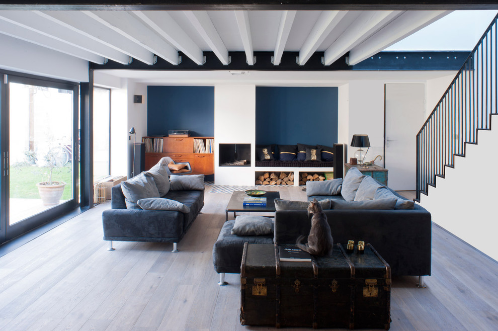 Idee per un grande soggiorno design chiuso con pareti blu, libreria, parquet chiaro, camino classico, cornice del camino in pietra e pavimento beige