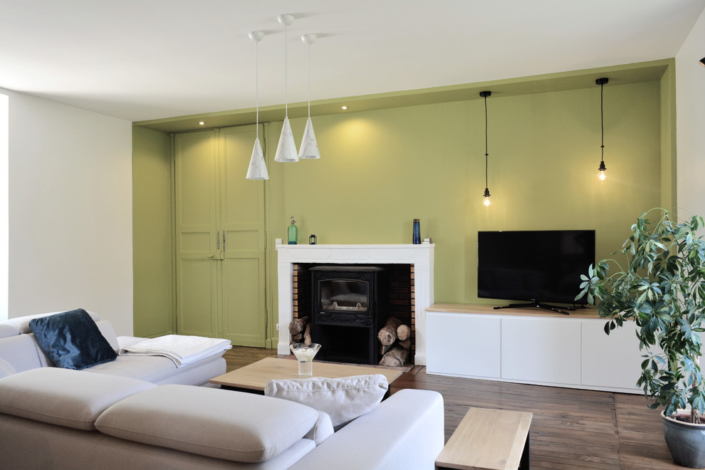 Modernes Wohnzimmer mit grüner Wandfarbe, dunklem Holzboden, Kaminofen, freistehendem TV und braunem Boden in Sonstige