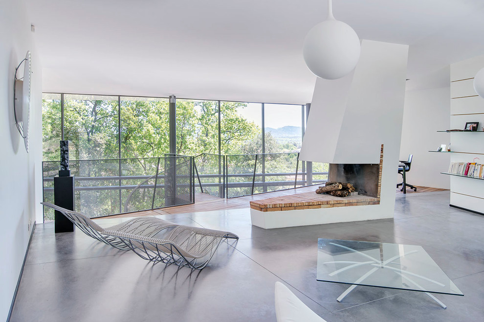 Contemporary open plan living room in Marseille with white walls, concrete flooring, a two-sided fireplace, a brick fireplace surround and grey floors.