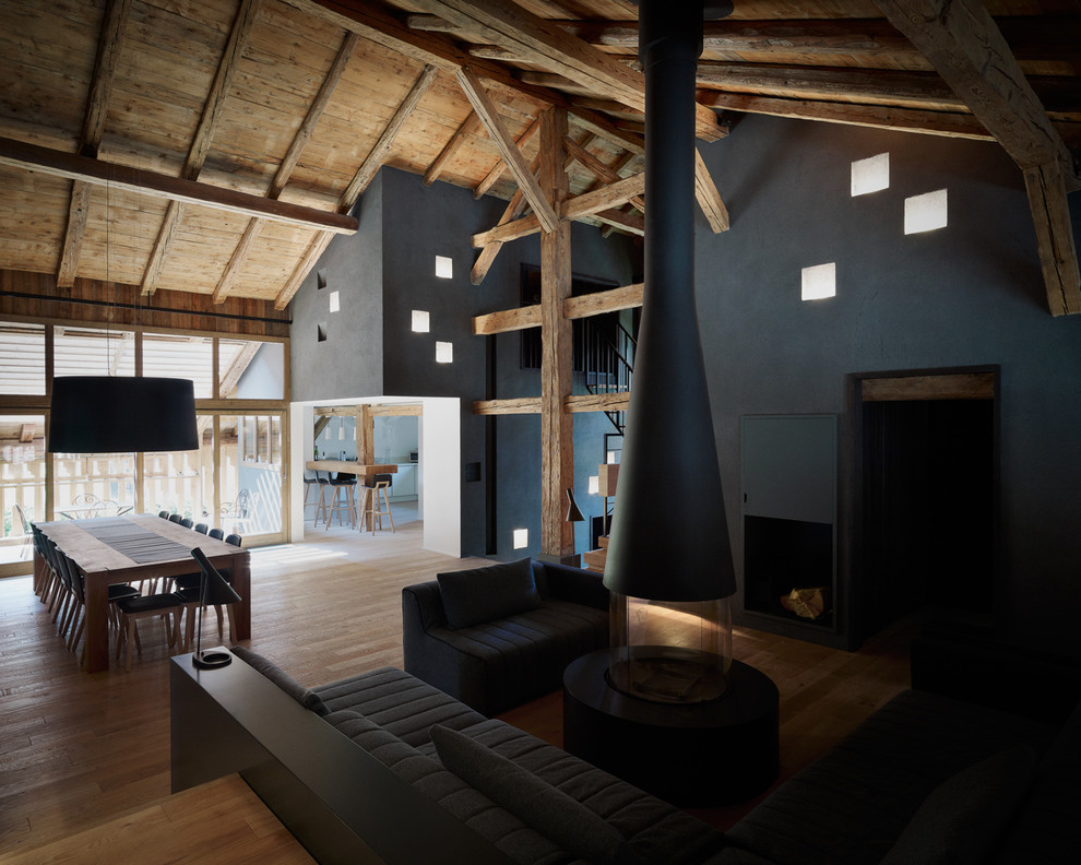 Idee per un soggiorno minimal con pareti nere, pavimento in legno massello medio, camino sospeso, cornice del camino in metallo e TV nascosta