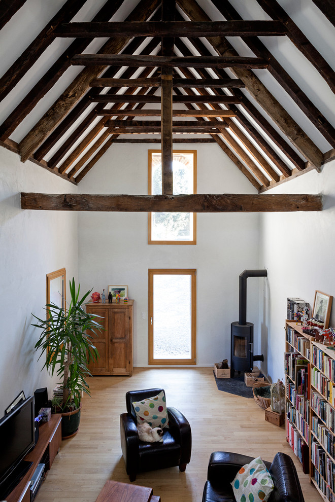 Immagine di un grande soggiorno country aperto con pareti bianche, parquet chiaro, stufa a legna, TV autoportante e libreria