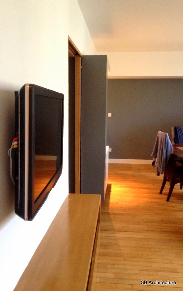 Cette photo montre un salon moderne ouvert avec un mur blanc, parquet clair et un téléviseur fixé au mur.