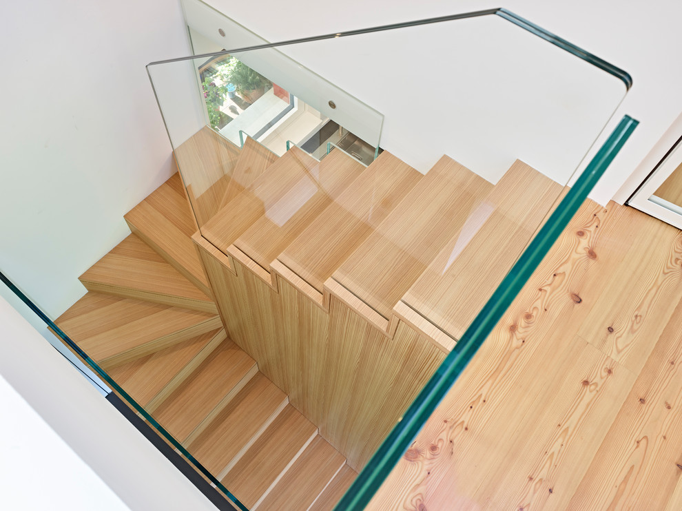 他の地域にあるコンテンポラリースタイルのおしゃれな折り返し階段 (木の蹴込み板、ガラスフェンス) の写真