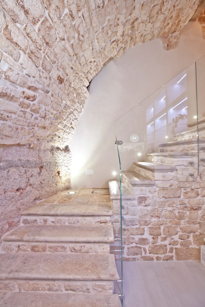 Ejemplo de escalera en L actual pequeña con escalones de piedra caliza, contrahuellas de piedra caliza y barandilla de vidrio