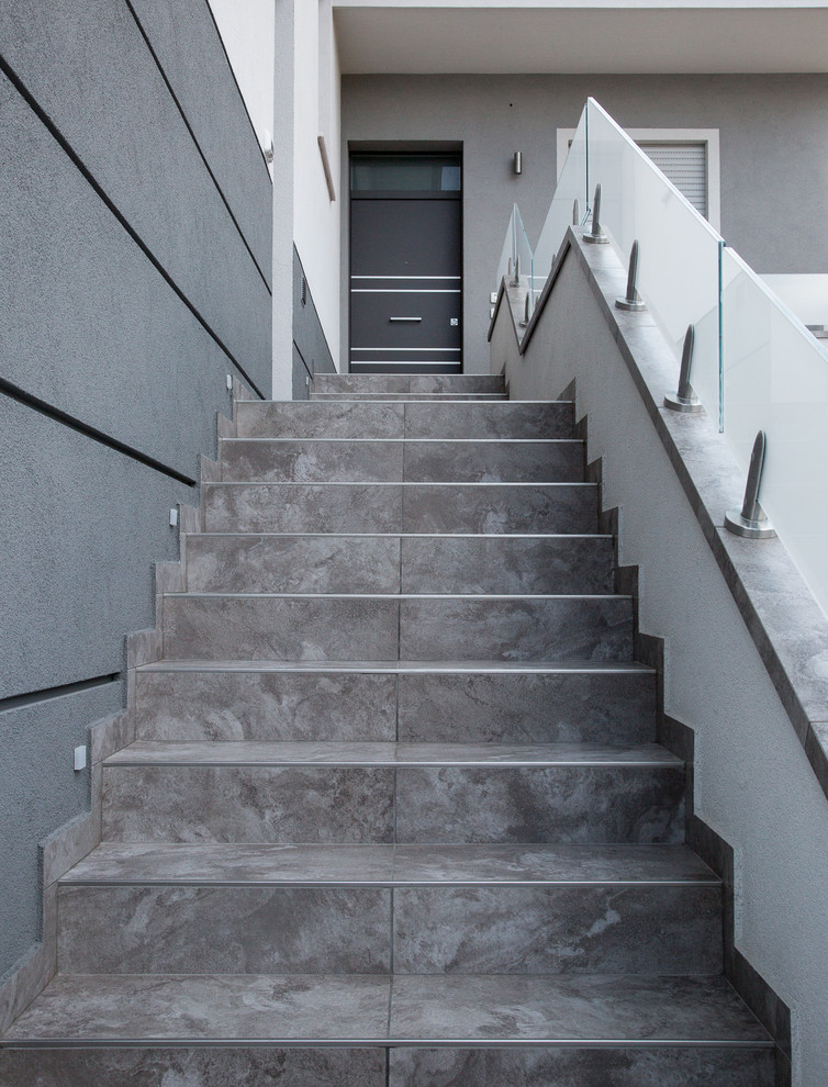 Свежая идея для дизайна: прямая лестница среднего размера в современном стиле с ступенями из плитки, подступенками из плитки и стеклянными перилами - отличное фото интерьера