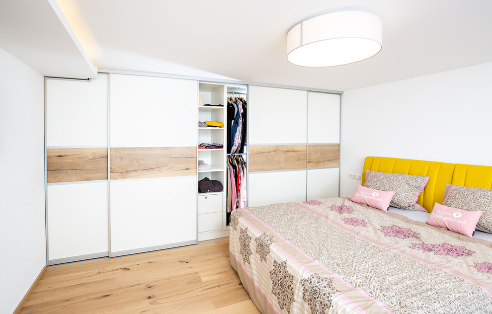 Modelo de dormitorio principal moderno grande con paredes blancas, suelo de madera en tonos medios y suelo marrón