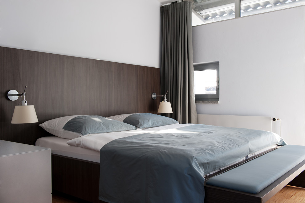 Modernes Hauptschlafzimmer ohne Kamin mit weißer Wandfarbe und braunem Holzboden in Dortmund