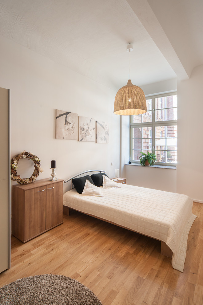 Großes Nordisches Schlafzimmer ohne Kamin mit weißer Wandfarbe und braunem Holzboden in Berlin