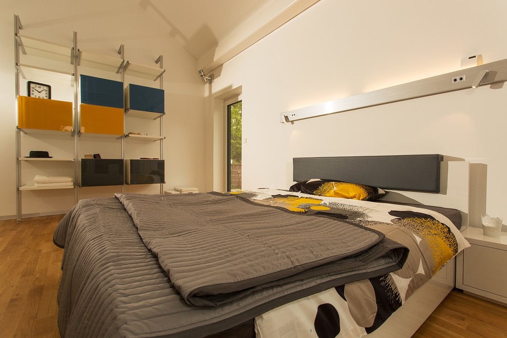 Modelo de dormitorio principal actual de tamaño medio con paredes blancas, suelo de madera en tonos medios y suelo marrón