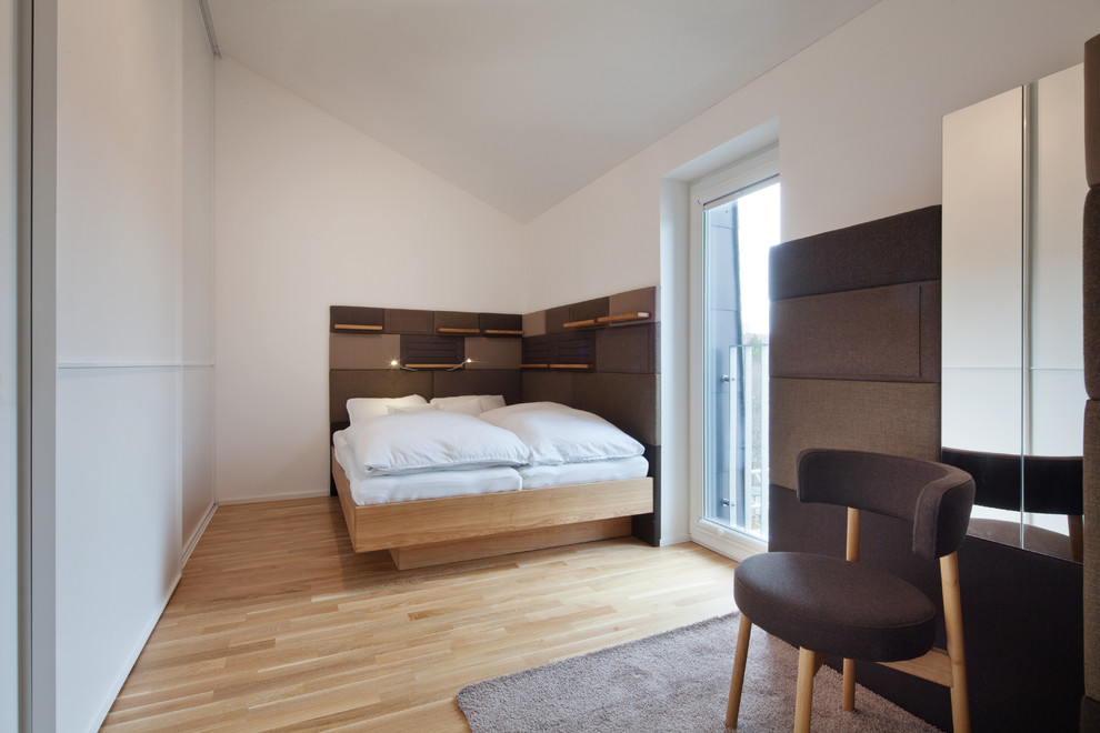 Modelo de dormitorio principal moderno grande sin chimenea con paredes blancas, suelo de madera clara y suelo beige