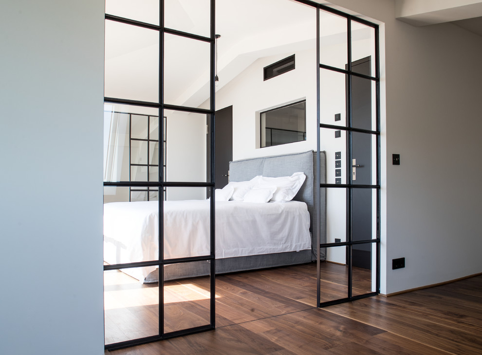 Ejemplo de dormitorio principal industrial de tamaño medio con paredes blancas y suelo de madera en tonos medios