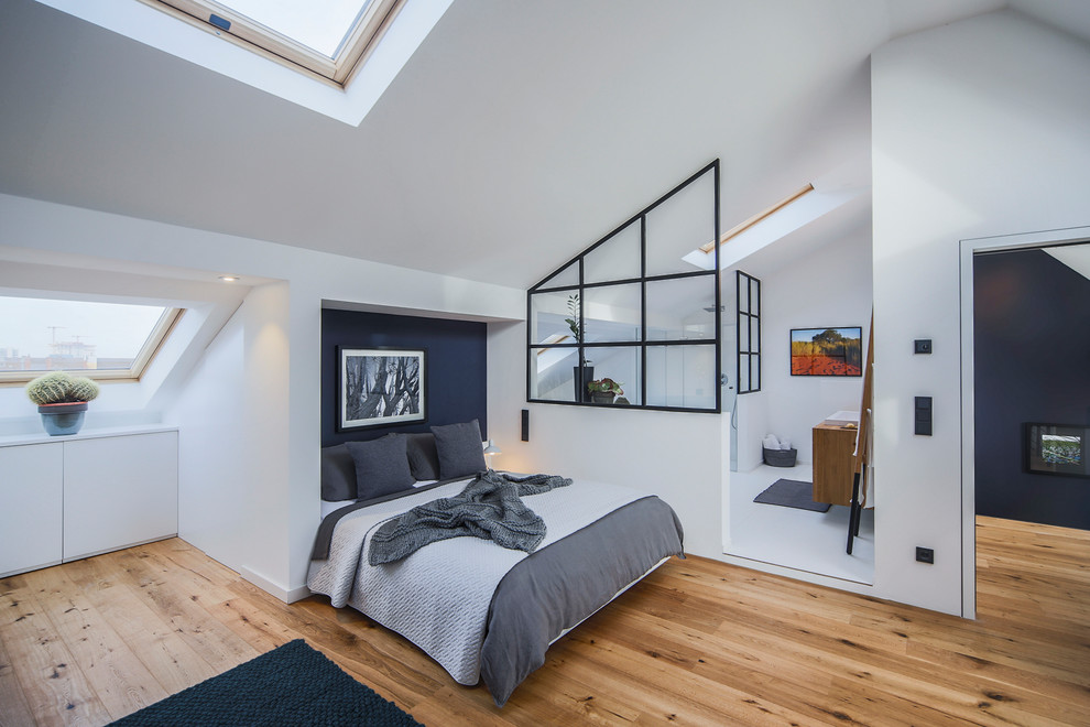 Mittelgroßes Industrial Schlafzimmer im Dachboden mit weißer Wandfarbe, braunem Holzboden und braunem Boden in Düsseldorf