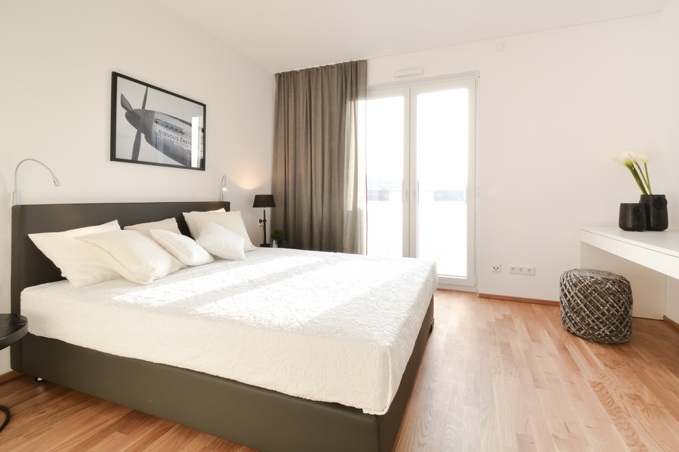 Diseño de dormitorio principal actual de tamaño medio sin chimenea con paredes blancas y suelo de madera en tonos medios