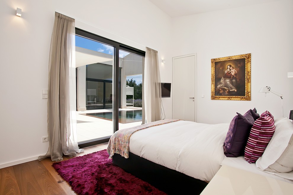 Imagen de dormitorio actual de tamaño medio sin chimenea con paredes blancas, suelo de madera en tonos medios y suelo marrón