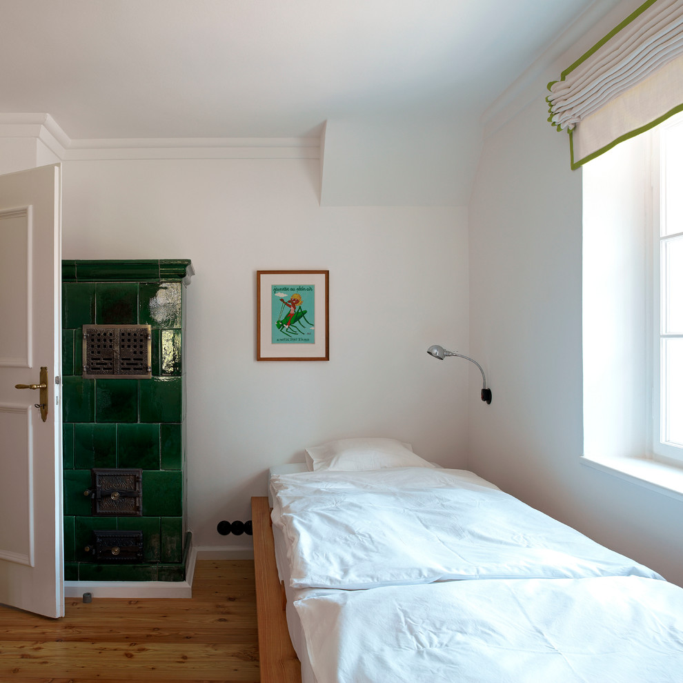 Kleines Landhaus Schlafzimmer mit weißer Wandfarbe, braunem Holzboden, Kaminofen und gefliester Kaminumrandung in München