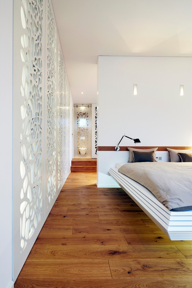 Mittelgroßes Modernes Hauptschlafzimmer ohne Kamin mit weißer Wandfarbe, braunem Holzboden und braunem Boden in Köln