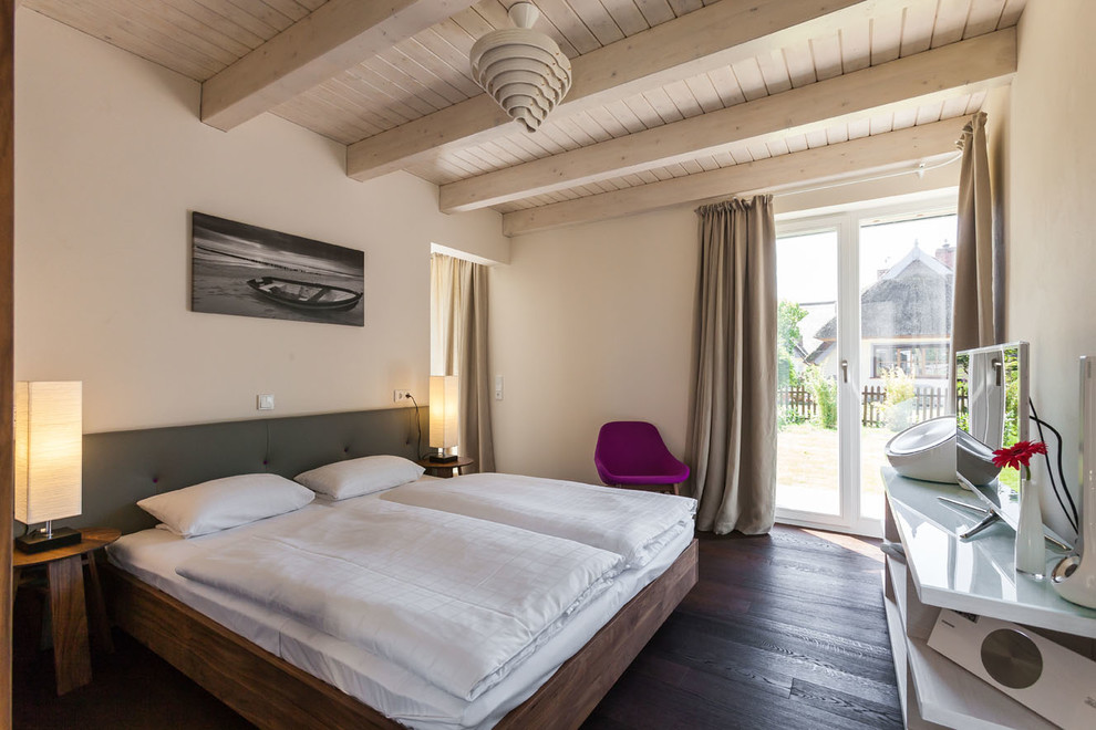 Imagen de dormitorio principal y televisión actual de tamaño medio sin chimenea con paredes beige y suelo de madera oscura