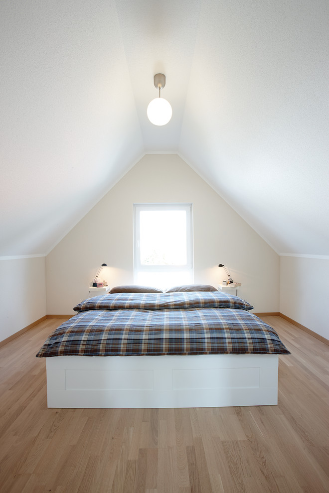 Imagen de dormitorio principal nórdico pequeño sin chimenea con paredes blancas, suelo de madera en tonos medios y techo inclinado