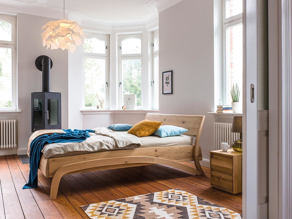 Mittelgroßes Skandinavisches Hauptschlafzimmer mit weißer Wandfarbe, gebeiztem Holzboden, Kaminofen und Kaminumrandung aus Metall in Bremen