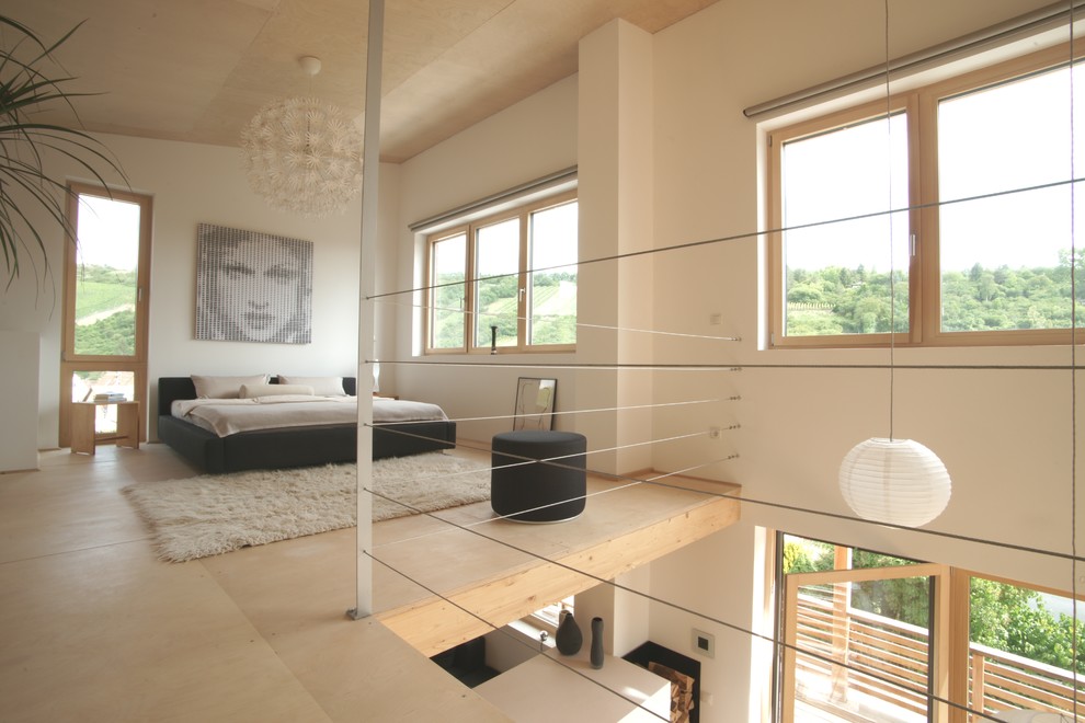 Imagen de dormitorio tipo loft actual de tamaño medio sin chimenea con paredes blancas, suelo de madera clara, suelo beige y madera