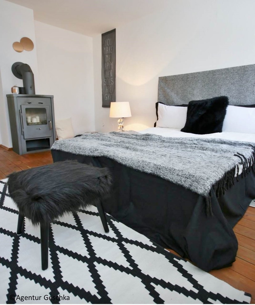Imagen de dormitorio escandinavo de tamaño medio con suelo de madera en tonos medios, paredes blancas, estufa de leña y marco de chimenea de metal