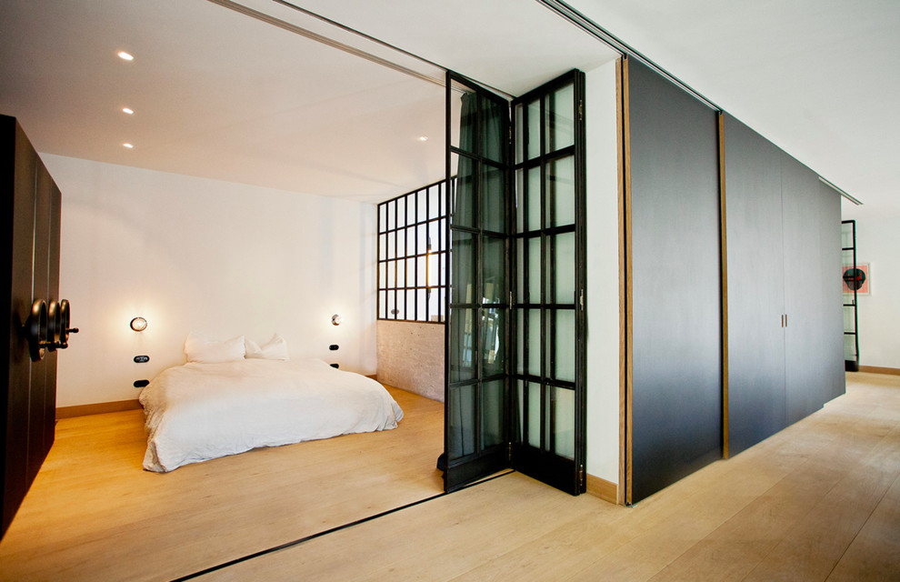 Ejemplo de dormitorio principal industrial grande sin chimenea con paredes blancas y suelo de madera en tonos medios