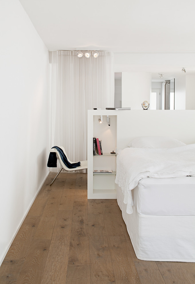 Diseño de dormitorio principal minimalista sin chimenea con paredes blancas y suelo de madera en tonos medios